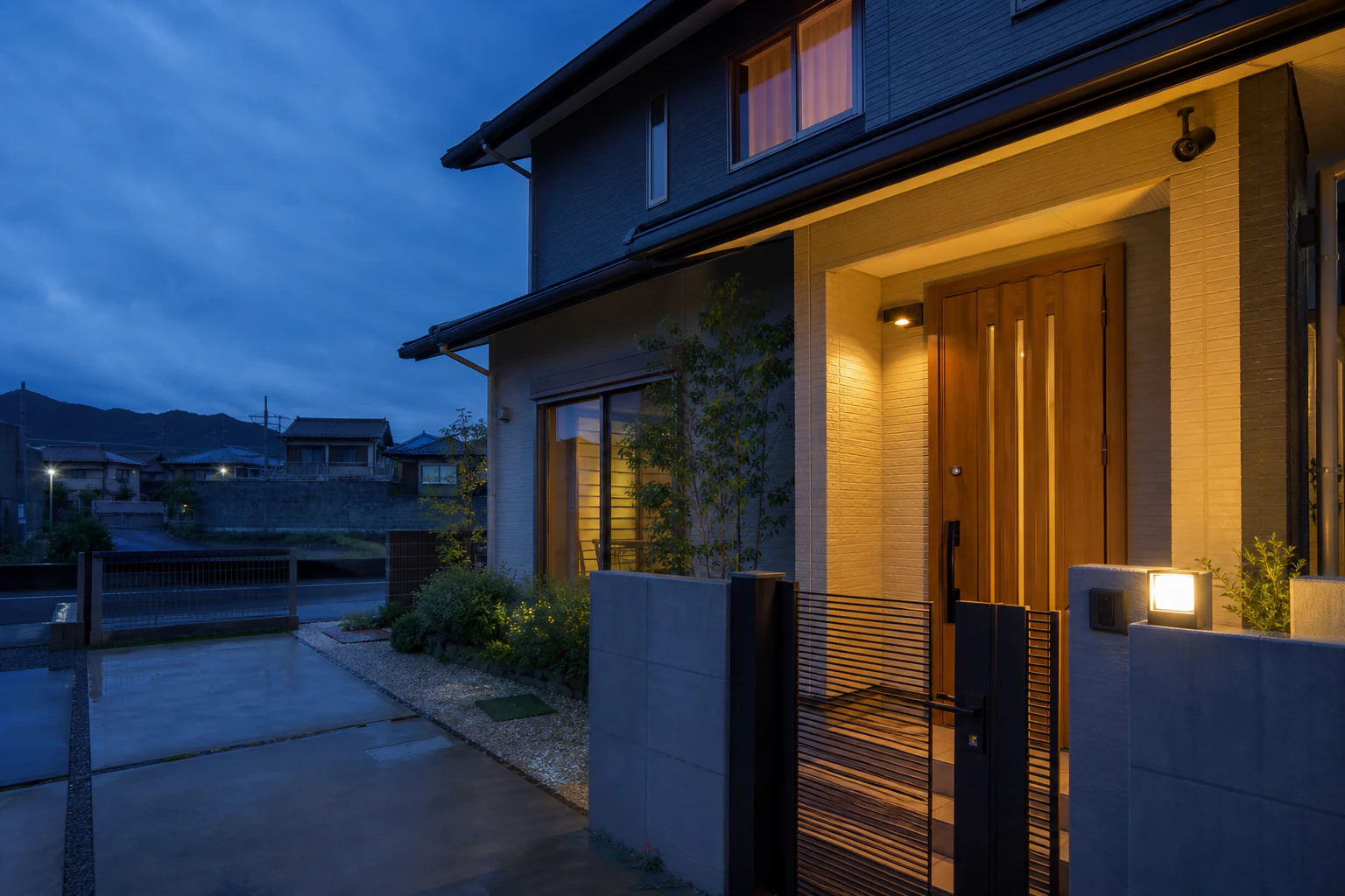 日本の戸建ての軒下に屋外カメラを設置し玄関と門まわりを見渡す夕方の風景