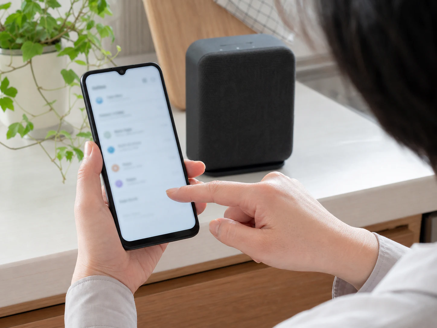 スマートホームの設定をスマートフォンで確認する手元と、奥に置かれたスピーカー